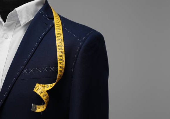 Semi-ready jacket with tailor's measuring tape on mannequin against grey background, closeup. Space for text