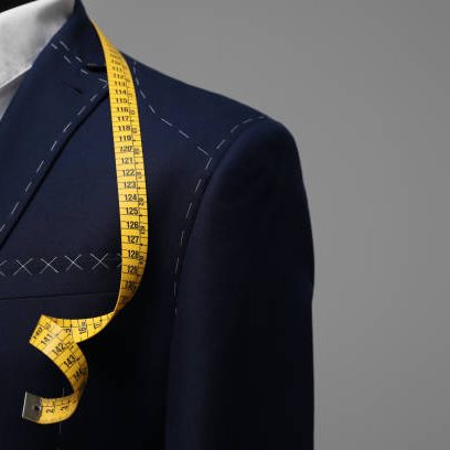 Semi-ready jacket with tailor's measuring tape on mannequin against grey background, closeup. Space for text